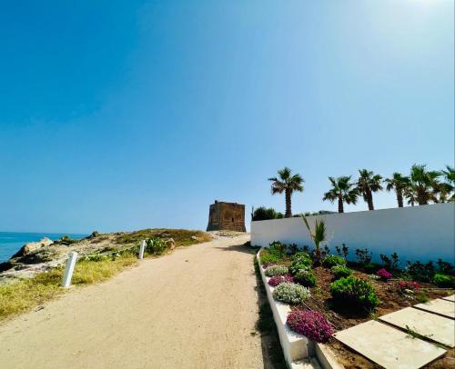 uma estrada de terra com flores e palmeiras numa praia em Torre Pozzillo Beach em Cinisi