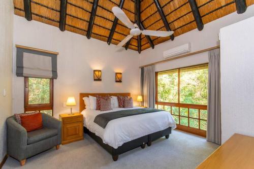 a bedroom with a bed and a chair and windows at Kruger Park Lodge Unit No. 308 in Hazyview