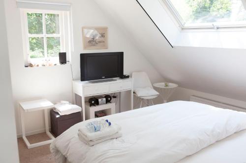 a white bedroom with a bed and a flat screen tv at Cottage Markdal in Breda