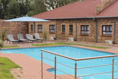 a swimming pool with chairs and an umbrella at EMPEROR LODGE AND TOURS in Germiston