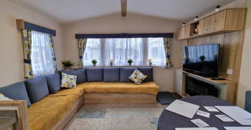 ein Wohnzimmer mit einem blauen Sofa und einem Fernseher in der Unterkunft Cwtch, White Horse, Seal Bay Resort in Selsey