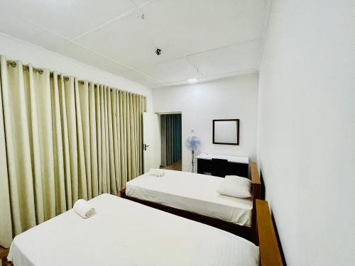 2 camas en una habitación con paredes y cortinas blancas en The Colombo Home en Nugegoda