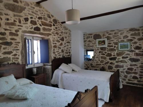 1 dormitorio con 2 camas y pared de piedra en Casa rural de piedra en una aldea tranquila de Zas 