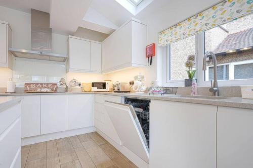 a white kitchen with white cabinets and a window at Beautiful House - Sleeps 8 - Close to City Centre with Free Parking, Fast Wifi and Smart TV with Virgin TV and Netflix by Yoko Property in Northampton