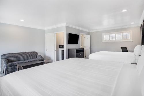 a white bedroom with two beds and a chair at Aura Inn Monterey in Monterey