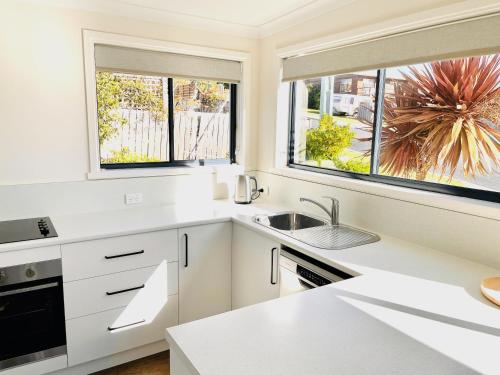 a white kitchen with a sink and two windows at Bays Rest in St Helens