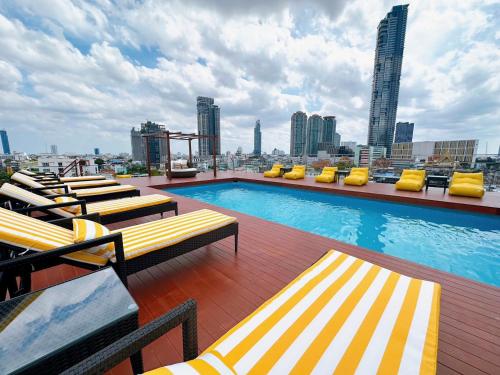 a rooftop swimming pool with lounge chairs and a city skyline at Miloft Sathorn Hotel in Bangkok
