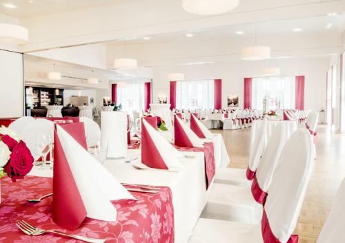 um salão de banquetes com mesas brancas e cadeiras vermelhas em Hotel Hilling em Papenburg