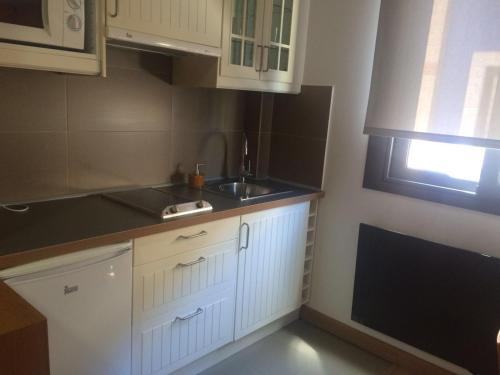 cocina con armarios blancos, fregadero y ventana en Alojamientos Maramar, en Candás