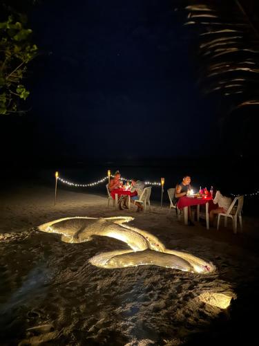 a group of people sitting at tables on the beach at night at Bougainvillea Inn - Maldives in Fulidhoo