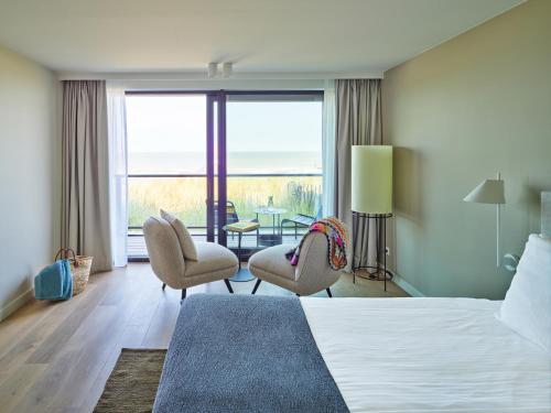 a hotel room with a bed and chairs and a large window at Hotel de Blanke Top in Cadzand-Bad