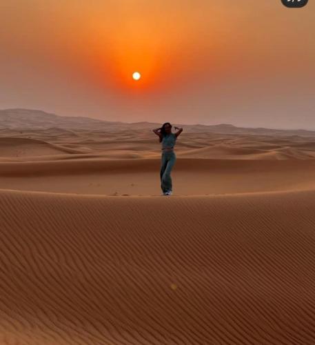 a woman standing in the desert at the sunset at Merzouga Top Luxury Camp in Merzouga