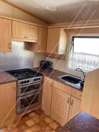 a kitchen with wooden cabinets and a stove top oven at 8 berth static caravan coral beach ingoldmells in Ingoldmells