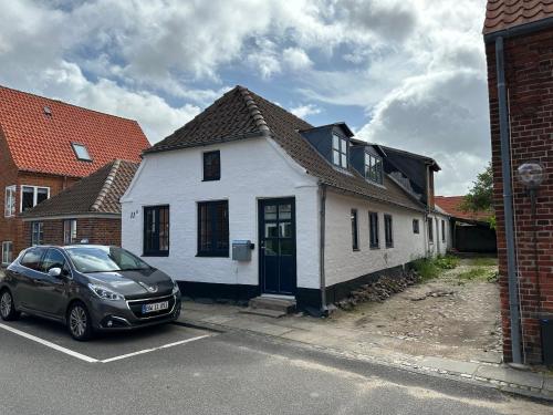 a white house with a car parked in a parking lot at Charmerende stue lejlighed i centrum in Ringkøbing