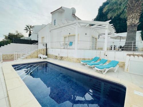 a swimming pool with two blue chairs and a house at Casa Evie in El Campello