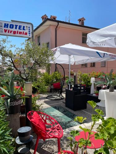 un patio con una silla roja, mesas y sombrillas en Hotel Virginia, en Garda