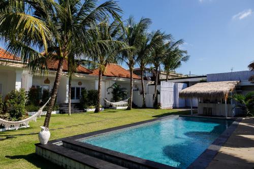 a swimming pool in front of a house with palm trees at Bella Bali in Uluwatu