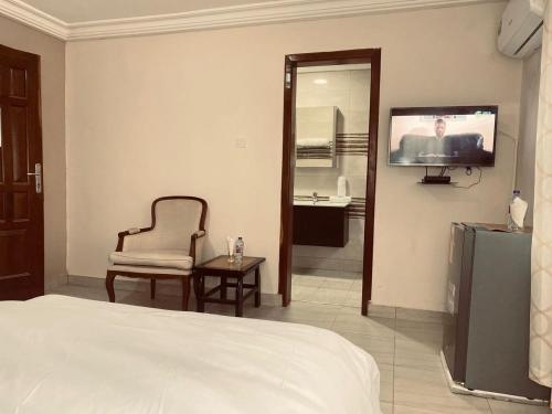 a bedroom with a bed and a tv and a chair at Joyous AP Guest House in Aburi
