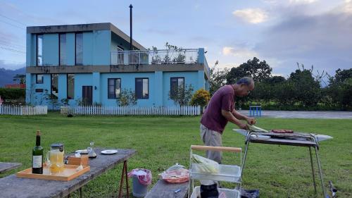 un hombre preparando comida en una parrilla frente a una casa en Kelly Field Homestay, en Guangfu