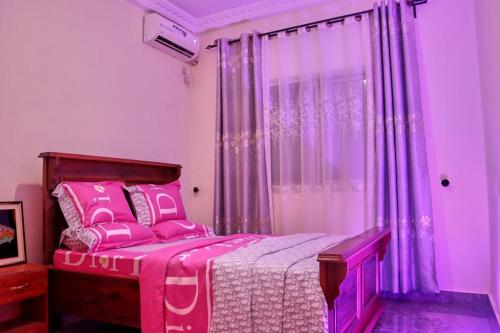 une chambre rose avec un lit avec des draps roses dans l'établissement J&B Home, à Kribi