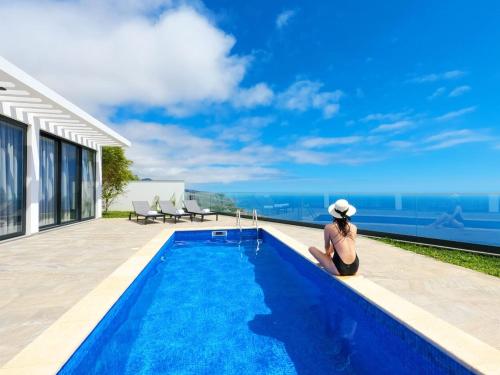 a woman sitting next to a swimming pool on a house at Villa Céu e Mar in Prazeres