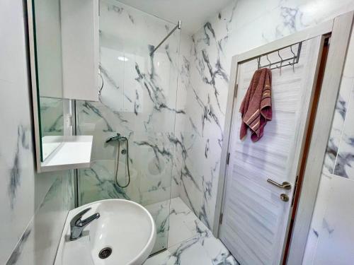 uma casa de banho branca com um lavatório e um chuveiro em BS Apartman em Podgorica