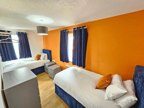a room with two beds and an orange wall at Amazing 4BR Near Hospital, Free Parking, Sleeps 10 in Laindon