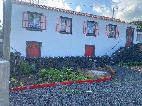a white house with red doors and a stone wall at PicoComigo in Lajes do Pico
