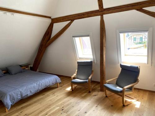 a bedroom with two chairs and a bed and two windows at triplex dans une ferme rénovée in Gals