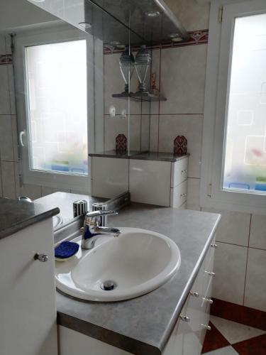 La salle de bains est pourvue d'un lavabo blanc et de 2 fenêtres. dans l'établissement Ty Pempoul - logement 2 chambres - 100 m de la plage, à Saint-Pol-de-Léon