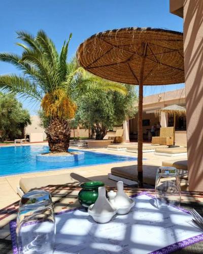 uma mesa com cadeiras e um guarda-sol ao lado de uma piscina em EL BAHJA HOTELL em Marraquexe