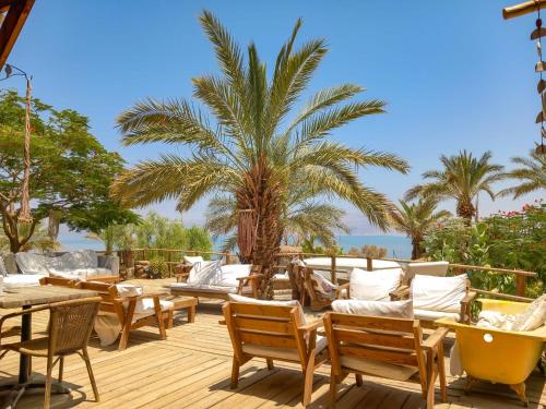 a deck with chairs and tables and a palm tree at Ein Gedi Camp Lodge in Ein Gedi