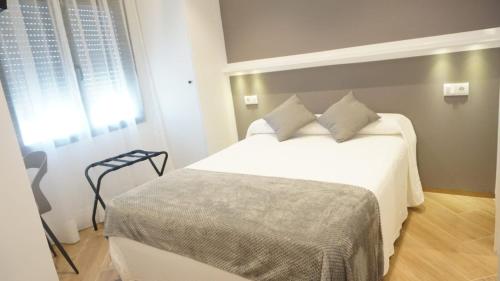 1 dormitorio con cama blanca y ventana en Hostal León en Torreorgaz