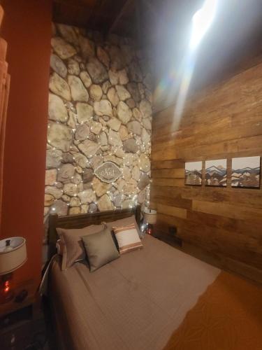 a bed in a room with a stone wall at Chalé Colorado Vibe in Camanducaia