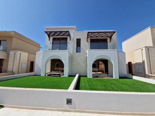 a large white house with a yard of green grass at Rivira Miko 2 in Salalah
