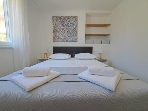 a white bedroom with a large bed with two pillows at Holiday house SeaDream - 50 meters from the sea in Brodarica