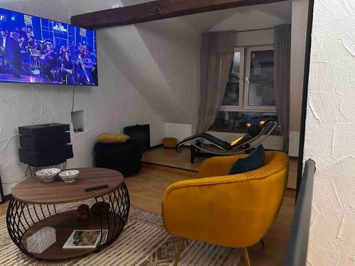 ein Wohnzimmer mit einem gelben Stuhl und einem TV in der Unterkunft Amina’s Auberge nähe Saarbrücken in Alsting