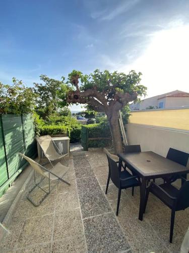 eine Terrasse mit einem Tisch, Stühlen und einem Baum in der Unterkunft Joli studio de vacances vue mer in Sausset-les-Pins
