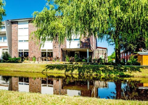 a building with a tree and a pond in front of it at Hotel Hilling in Papenburg