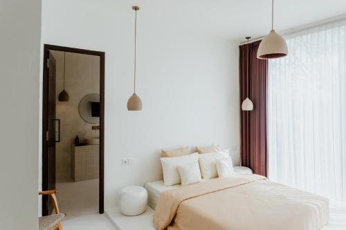 a white bedroom with a bed and a mirror at The Hut Hut in Uluwatu