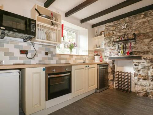 a kitchen with white cabinets and a stone wall at Middleway Cottage in Saint Blazey