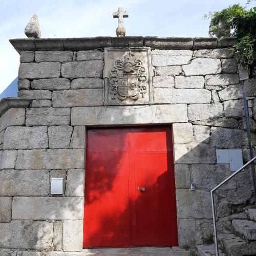 a red door in a stone building with a cross at Casa do Loureiro in Paradela