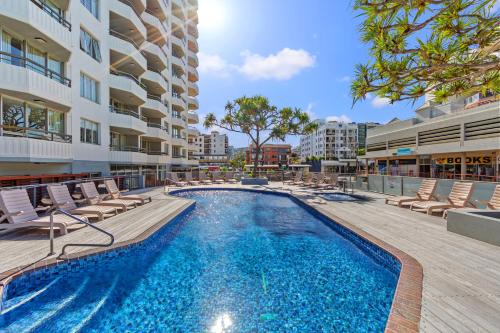 a swimming pool with lounge chairs and a building at Newport Mooloolaba Apartments in Mooloolaba