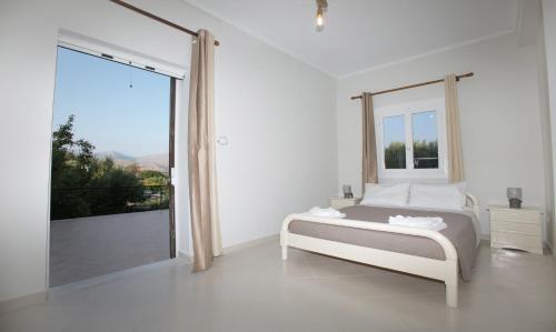 ein weißes Schlafzimmer mit einem Bett und einem großen Fenster in der Unterkunft BABI'S VILLA - Garden apartment in Lixouri
