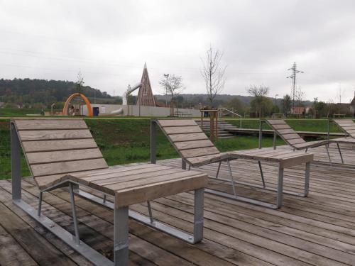 three wooden benches sitting on a deck with a playground at La Campagne à la ville dans pavillon avec jardin Clos et privatif in Héricourt