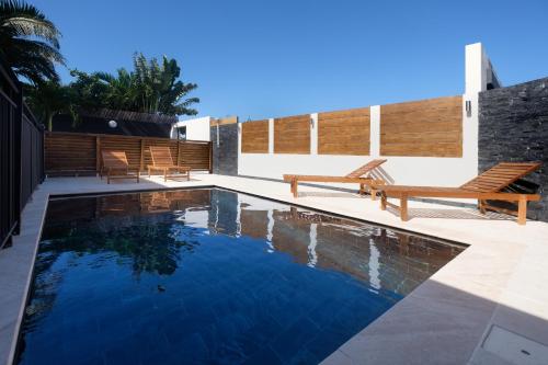 a swimming pool with two wooden benches next to a house at Villa Cap Noir piscine chauffée avril à octobre in Saint-Joseph