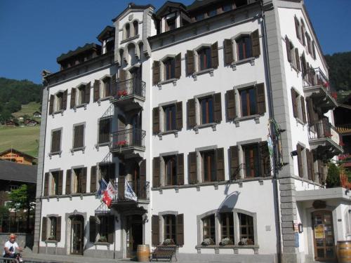 Un grand bâtiment blanc avec des drapeaux devant lui dans l'établissement Auberge de la Bourgeoisie, à Troistorrents