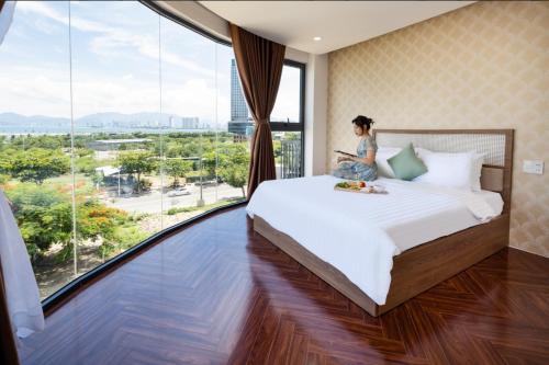 a woman sitting on a bed in a room with a large window at MYDO Condotel in Nha Trang