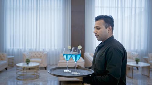 a man holding a tray with two glasses of wine at Mayur Belgaum Presidency Hotel & Spa in Belgaum