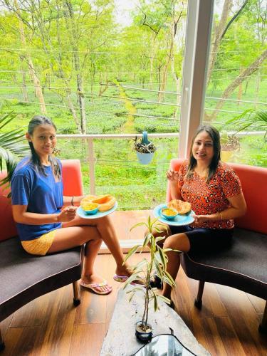two women sitting in a room with plates of food at Homestay by the Tea Garden Dibrugarh in Dibrugarh